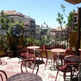 Terraza de verano en Madrid, con mesas y sillas rojas, ventilador y vistas a edificios históricos. Un lugar perfecto para el viajero madrileño.