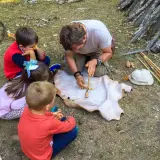 Un hombre enseña a niños a hacer fuego con un arco y un trozo de cuero. ¡Una aventura en la naturaleza para los más pequeños!