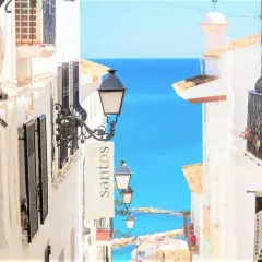 Calle empedrada con vistas al mar azul. Farolas y balcones floridos invitan a descubrir las cosas que hacer en Altea.