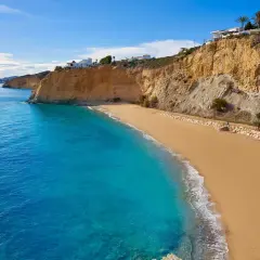 Arena dorada y aguas turquesas en la playa de Villajoyosa, con acantilados y casas blancas al fondo.