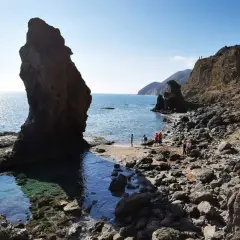 Gente disfrutando de la **playa del Sombrerico**, con sus rocas y aguas cristalinas. ¡Un lugar para guardar en la memoria!