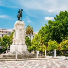 Majestuoso monumento ecuestre, una de las **estatuas en Sevilla**, rodeado de árboles frondosos y un cielo azul vibrante.
