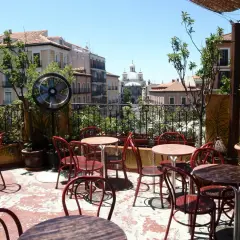Terraza de verano en Madrid, con mesas y sillas rojas, ventilador y vistas a edificios históricos. Un lugar perfecto para el viajero madrileño.