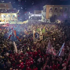Multitud celebrando con confeti y banderas en una calle por la noche.