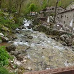 Río caudaloso y rocoso fluye hacia un pueblo de piedra con un cartel que dice "Bar Bulnes Comidas". ¡Así se llega a Bulnes!