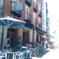 Gente disfrutando en las mesas exteriores del restaurante El 7 Vitoria, bajo un gran parasol azul.