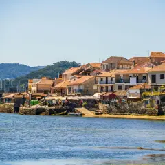 Pueblos de las Rías Baixas con casas de tejados naranjas junto al mar azul, un día soleado.
