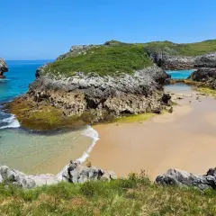 Una cala asturiana con aguas turquesas y arena dorada, rodeada de acantilados verdes. Un paraíso entre las playas más bonitas de Asturias.