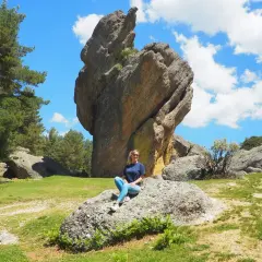 Una mujer sonríe sentada en una roca en un paisaje rocoso y verde. ¡Un lugar increíble que ver en Soria!