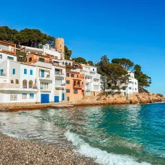 Casas blancas y coloridas se asoman al mar turquesa en la costa brava españa. Una pequeña playa de guijarros recibe las olas.