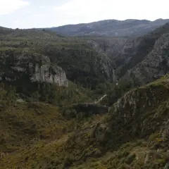 Paisaje montañoso con vegetación verde y rocas escarpadas. El **barranc de l'infern** se abre paso entre las colinas, con un camino serpenteante.