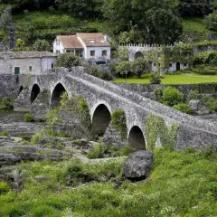 Puente de piedra cubierto de hiedra, con casas tradicionales al fondo. Un lugar idílico para visitar, así es como ponte Maceira como llegar.
