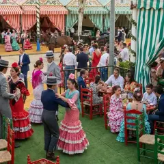 Gente vestida de flamenca baila y socializa en una feria, evocando la esencia de la feria de Sevilla en Madrid.