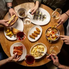 Amigos disfrutan tapas variadas: sándwich, croquetas, sardinas, gambas y pastel salado. ¡Un festín para saber donde comer bien y barato en Talavera de la Reina!