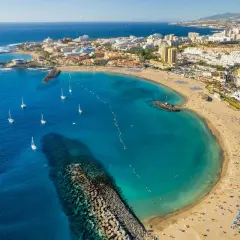 Vista aérea de una bahía con aguas turquesas, veleros y una playa repleta de gente, un ejemplo de las mejores playas Tenerife.