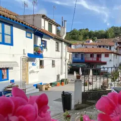 Casas blancas con detalles azules, tejados rojos y flores rosadas en un día soleado. Un vistazo a los encantadores pueblos cerca de Cudillero.