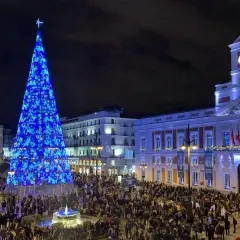 Gran árbol de Navidad azul ilumina la Puerta del Sol, llena de gente, ideal para planes de Navidad en Madrid.