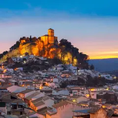 Pueblo blanco andaluz con castillo iluminado en la colina. Un lugar encantador que ver cerca de Granada al atardecer.