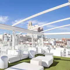 La terraza de Oscar, un oasis blanco con sofás modulares y césped artificial, ofrece vistas urbanas bajo un cielo azul.