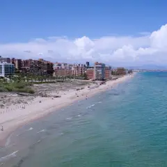 Vista aérea de la playa los Arenales con edificios residenciales al fondo y el mar turquesa.