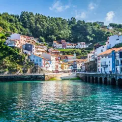 Pueblo costero con casas de colores en una ladera verde, un puerto y aguas turquesas. Un ejemplo de los lugares más bonitos de España.