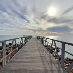 Muelle de madera sobre el mar, con cielo nublado y sol brillante. Un lugar ideal para disfrutar de la playa de Chilches.