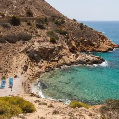 La cala Tío Ximo, con sus aguas turquesas y rocas doradas, invita a relajarse bajo el sol.