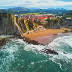 Impresionantes paisajes del País Vasco: acantilados, playa dorada y el mar Cantábrico rompiendo en rocas.