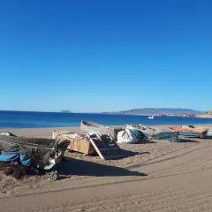 Barcas de pesca cubiertas en la arena de las playas de Mazarrón, con el mar azul y montañas al fondo.