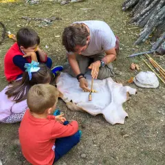 Un hombre enseña a niños a hacer fuego con un arco y un trozo de cuero. ¡Una aventura en la naturaleza para los más pequeños!