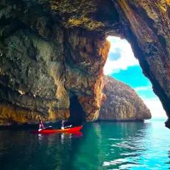 Dos personas en kayak exploran la Cova del Llop Mari en Jávea, con aguas turquesas y formaciones rocosas impresionantes.