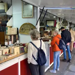 Gente buscando tesoros literarios en la feria del libro antiguo de Madrid. Estanterías repletas de tomos esperan ser descubiertos.