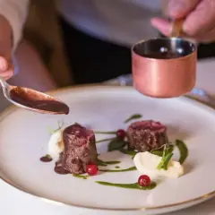 Chef decora un plato de carne con salsa en la granja Madrid.