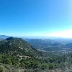 Un excursionista disfruta de la vista panorámica desde el balcon de Alicante, un paisaje montañoso cubierto de pinos bajo un cielo azul intenso.