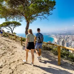Pareja camina hacia la Cruz de Benidorm, con vistas a la ciudad y la playa.