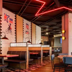 Interior de restaurante con cabinas, mesas y decoración moderna. Las paredes tienen murales inspiradores, como "Think Big". Las luces rojas de neón añaden un toque vibrante. Ideal para leer reseñas de Foster's Hollywood.