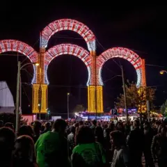 Noche de luces y alegría en las fiestas de Boadilla del Monte. Arcos luminosos decoran la entrada a un evento multitudinario.