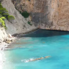 Aguas turquesas bañan la cala racó del corb, rodeada de imponentes acantilados y vegetación verde.