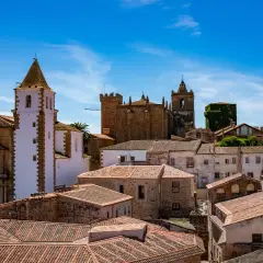Vistas de tejados y edificios históricos, incluyendo iglesias con torres blancas y campanarios, bajo un cielo azul. Un lugar ideal que ver en Cáceres provincia.