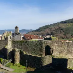 Ruinas de un castillo de piedra, con tejados rojos y colinas verdes al fondo. Un ejemplo de los pueblos bonitos cerca de Monforte de Lemos.