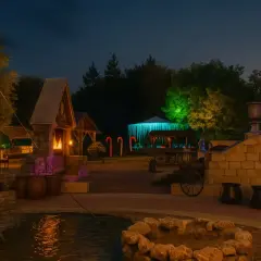 Un lugar mágico donde las luces iluminan el camino hacia el manantial de los sueños. Cabañas rústicas, un estanque y decoraciones festivas crean un ambiente encantador.