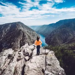 Niña en el mirador de Vilouxe, contemplando un cañón con un río azul y montañas verdes bajo un cielo nublado.