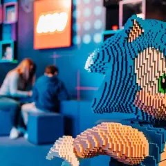 Figura de Sonic hecha de LEGO en el museo LEGO de Madrid. Al fondo, dos personas observan una exposición.