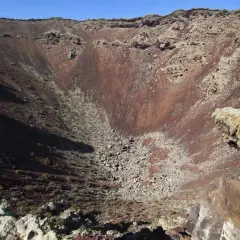 Interior del cráter del Volcán de la Corona, con rocas rojizas y vegetación escasa.