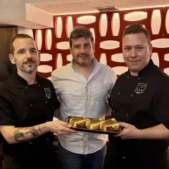 Tres hombres posan con un plato de aperitivos en un mesón. Las fotos capturan el momento.