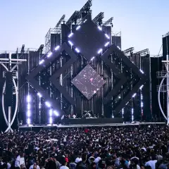 Multitud vibrante en un festival de música, escenario futurista con luces y pantallas. Una escena épica para tu summer story 2026.