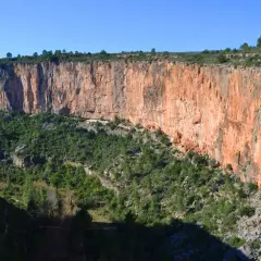 Impresionante pared rocosa anaranjada en la ruta de los calderones Chulilla, con vegetación verde cubriendo el fondo del cañón.