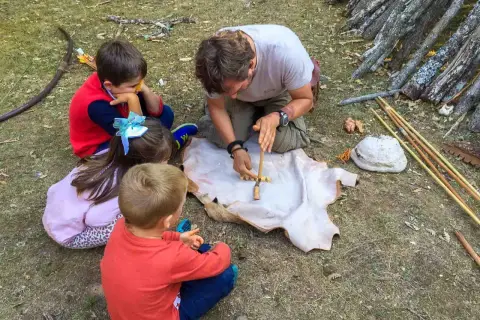Un hombre enseña a niños a hacer fuego con un arco y un trozo de cuero. ¡Una aventura en la naturaleza para los más pequeños!