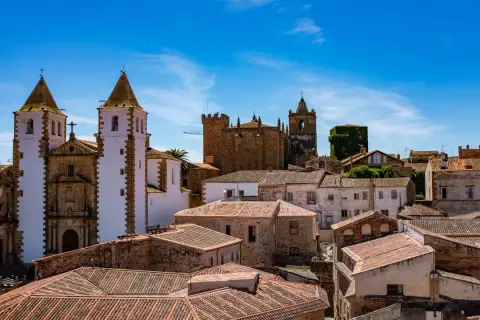 Vistas de tejados y edificios históricos, incluyendo iglesias con torres blancas y campanarios, bajo un cielo azul. Un lugar ideal que ver en Cáceres provincia.
