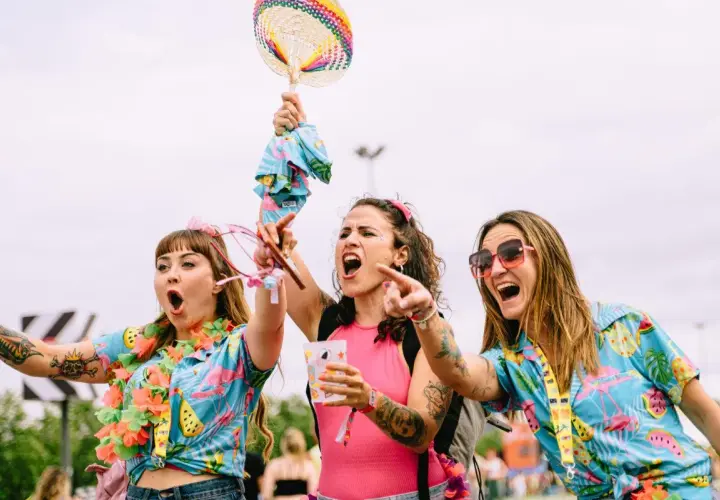 Tres chicas con camisas tropicales y collares de flores, riendo y bailando. ¡Me encanta el espíritu de las tuenti's!